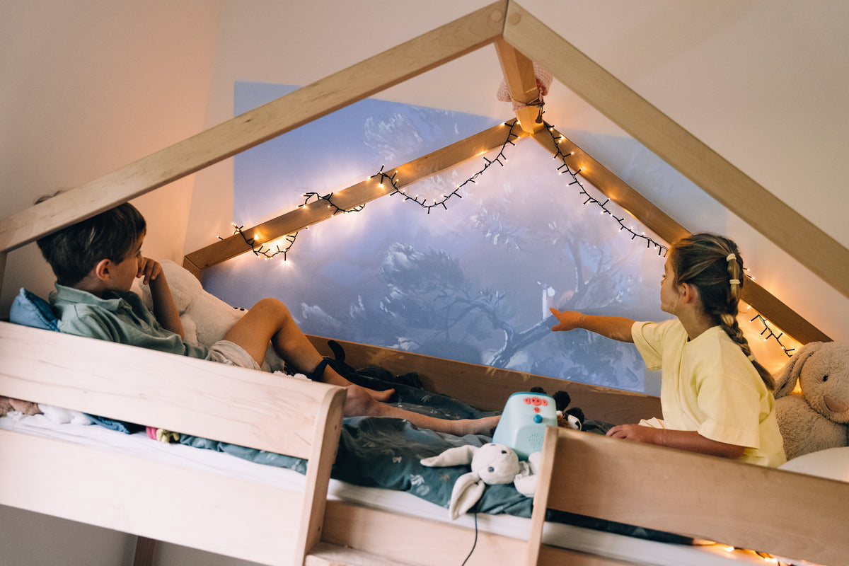 Des enfants dans un lit cabane regardent une histoire Tikino projetée au mur